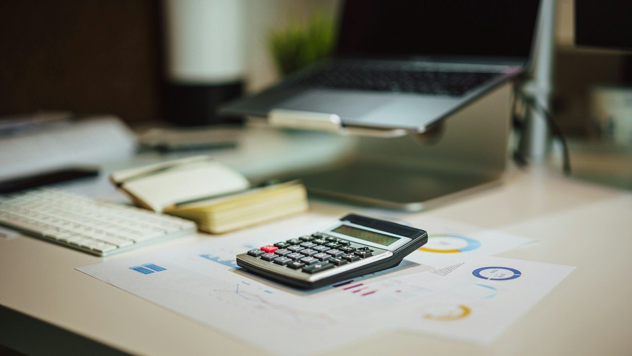 A calculator on printed charts beside a keyboard and notebook on an office desk