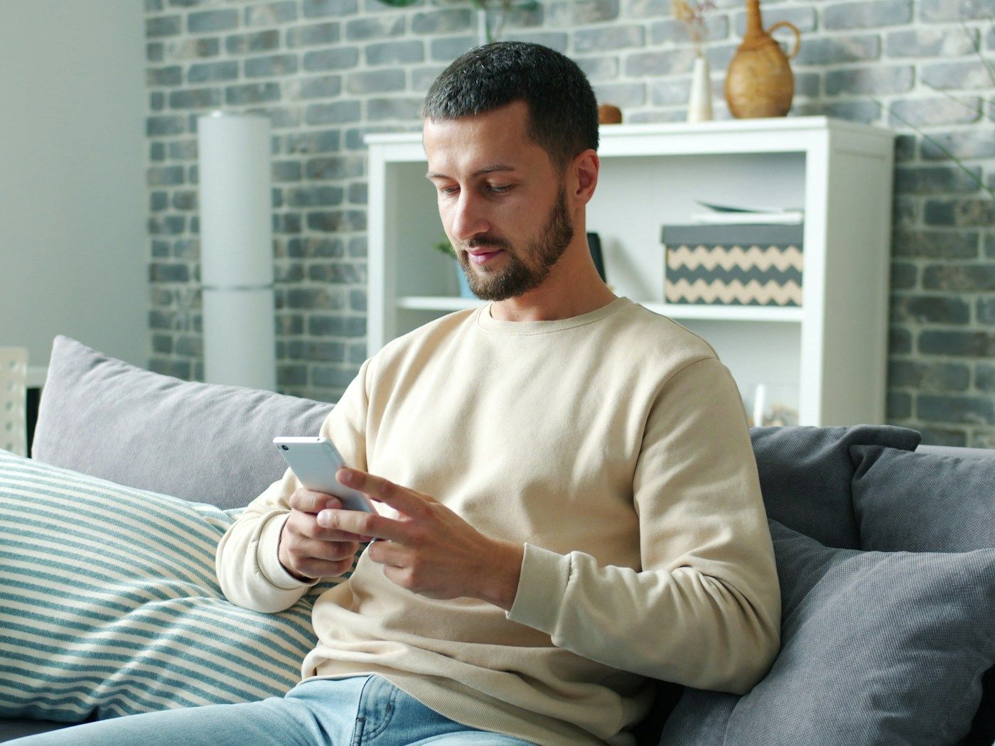 A man sits on a sofa at home typing a message on his phone
