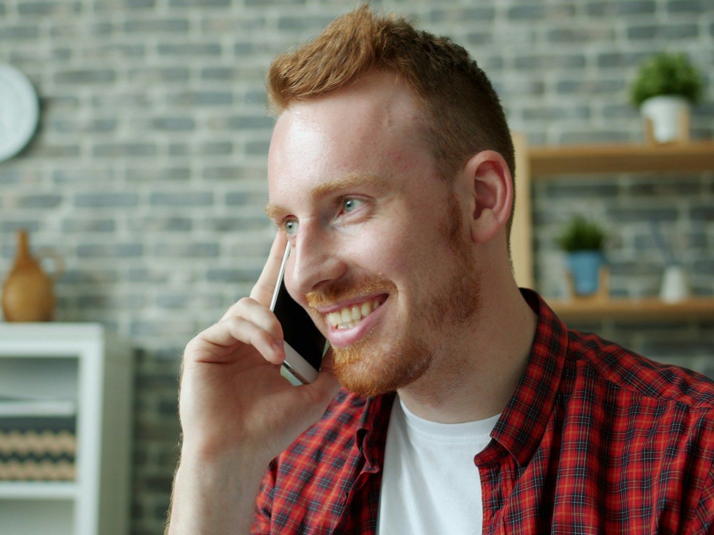 Photo: Vitaly Gariev on Unsplash A smiling man with red hair talks on his phone in a bright room