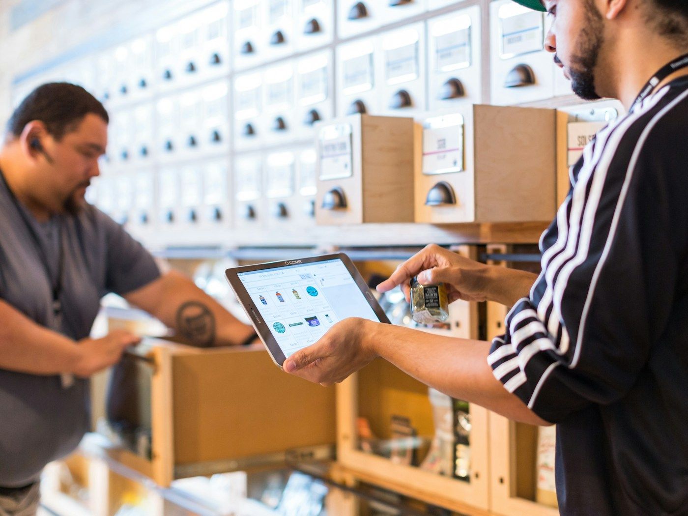 Photo: Cova Software on Unsplash Two men check an order on a tablet beside a wall of labelled storage drawers